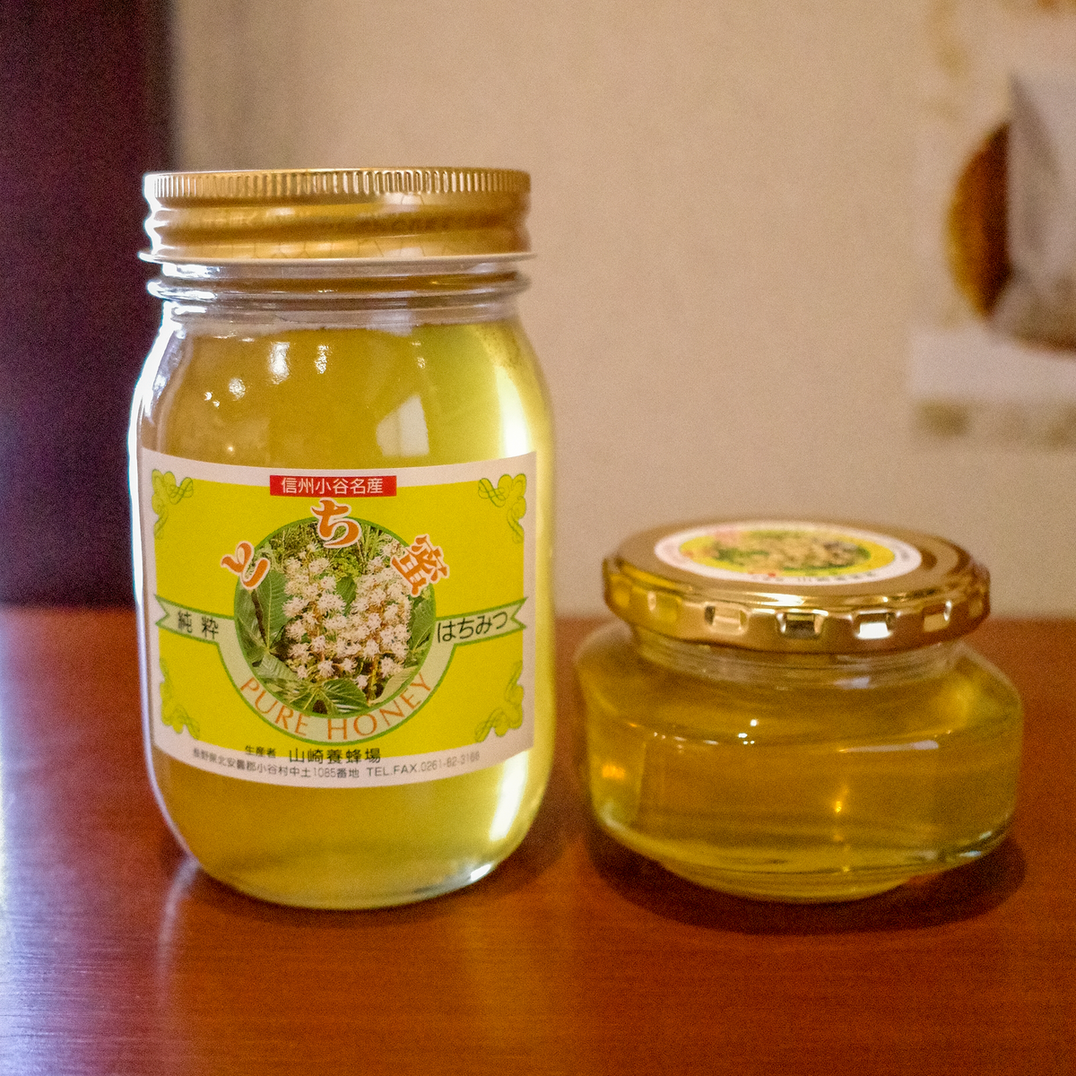 山崎養蜂場のとちみつ。木の棚に並ぶ大きい瓶と小さい瓶（販売商品は600gの大きい瓶です）